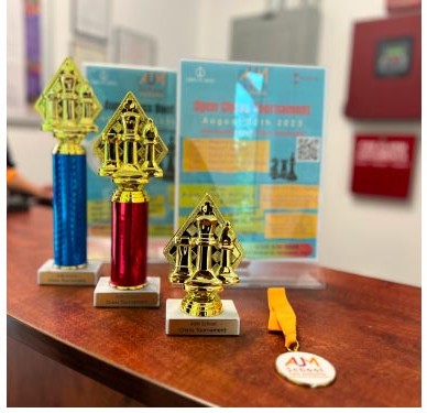 Chess tournament trophies and an Aum School medal displayed on a wooden table