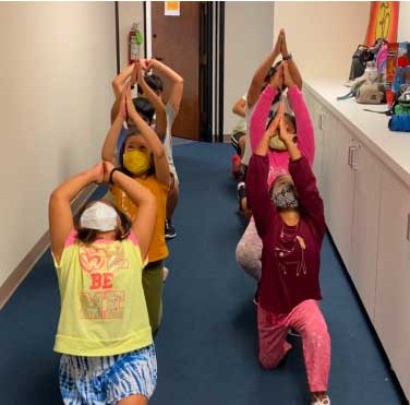Children practicing yoga poses in an Aum School classroom hallway